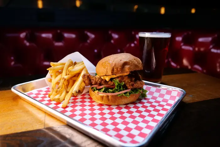 This is a photo of a fried chicken sandwich with a side of fries and a beer.